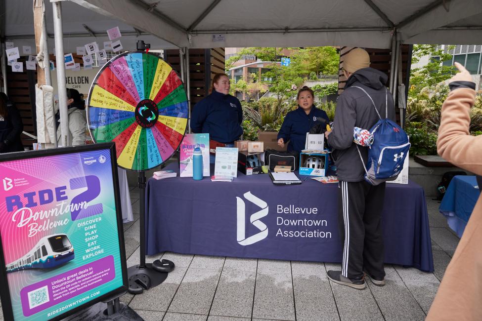 BDA reps stand in front of a booth with a prize wheel and promotional poster for their Ride2Downtown campaign