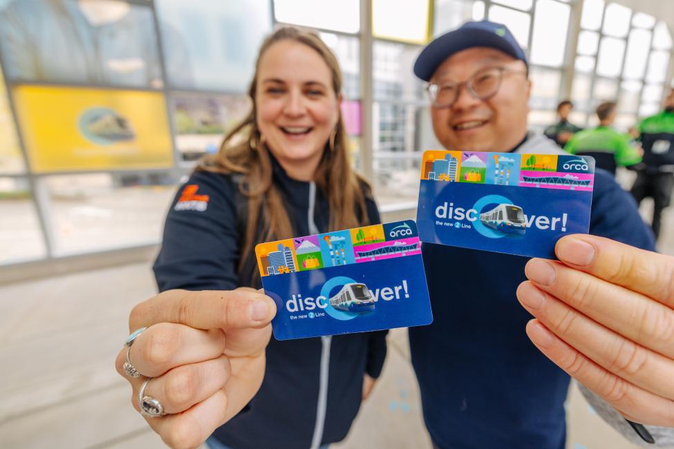 Two passengers hold up the 2-Line commemorative ORCA card