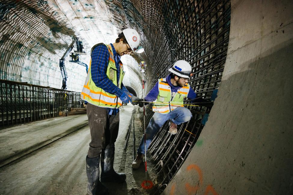 Two construction workers measure the wall of the tunnel under Downtown Bellevue.