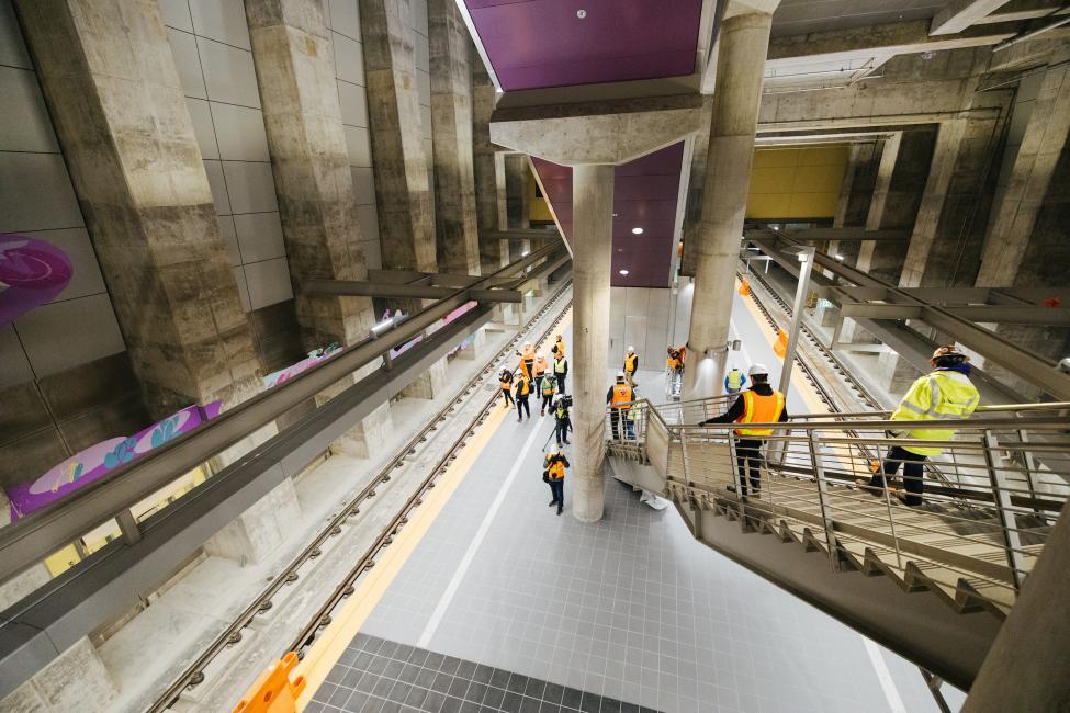 A group of people in orange vests walk down the stairs and around the platform at Roosevelt Station.