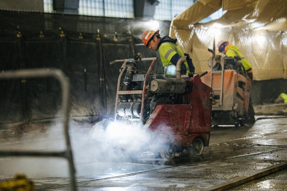 Workers in the construction area south of International District/Chinatown Station using machinery to remove concrete for new rails. 