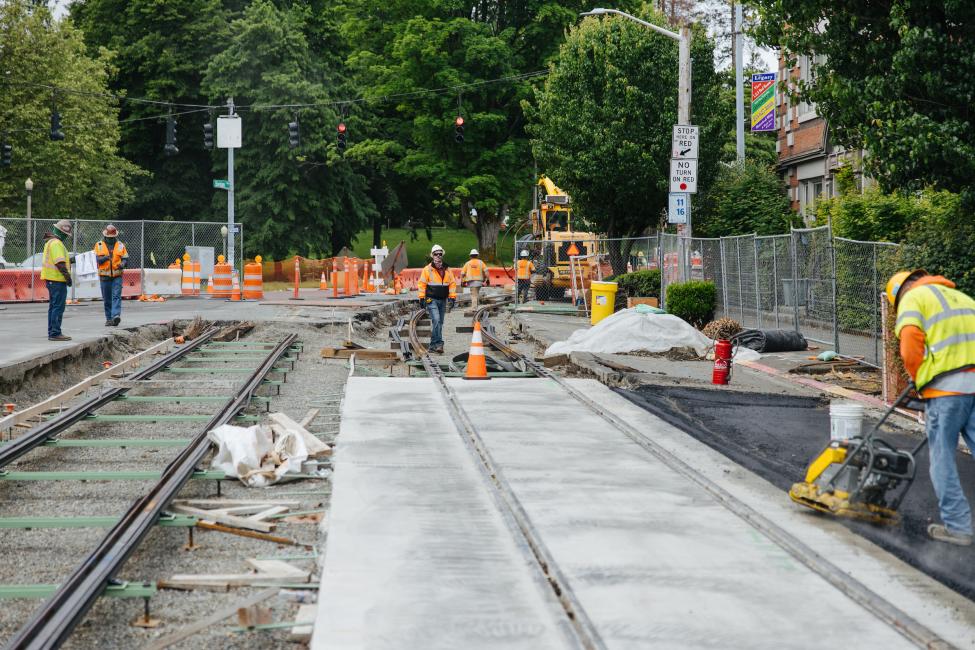 Workers lay cement around new train tracks in the street for the Hilltop Tacoma Link Extension. 