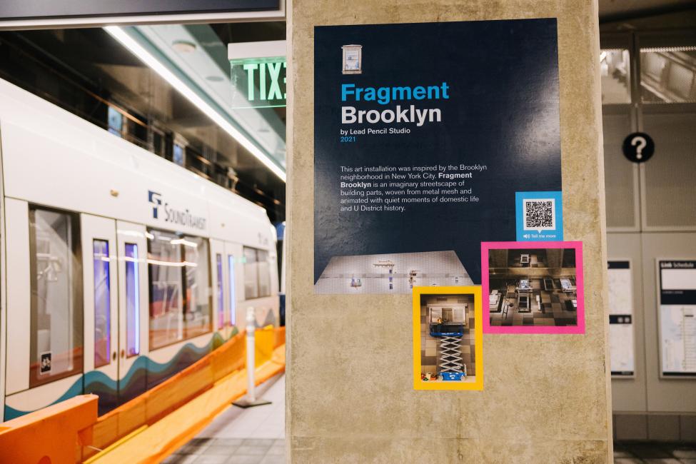 A sign on the platform at U District Station describes the art piece "Fragment Brooklyn."