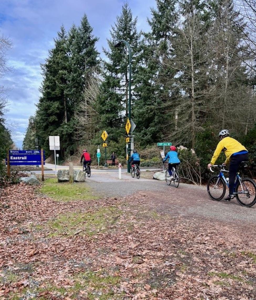 A group of cyclists pass a blue sign that reads 'Eastrail'