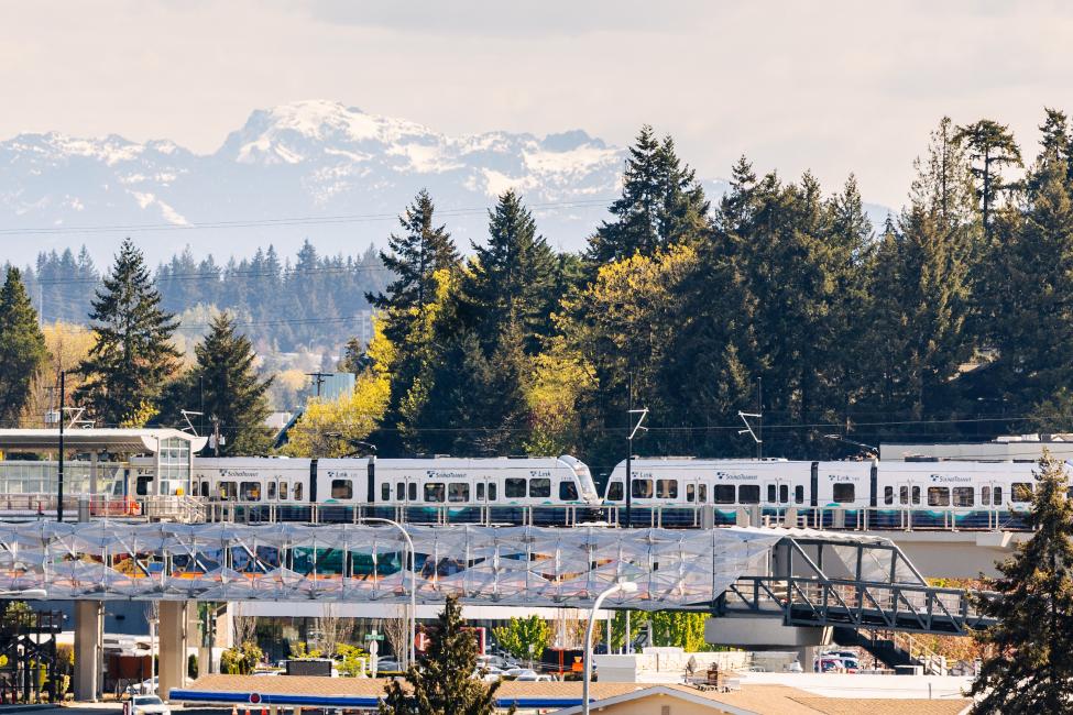A 2 Line train at Wilburton Station, with trees and mountains in the background and the nearby pedestrian bridge in the front