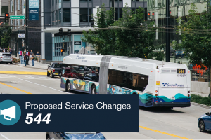A bus travels through downtown Seattle streets. A banner reads "Proposed Service Changes - 544."