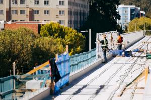 Two workers on an elevated light rail guideway in downtown Redmond, with green trees in the background. 