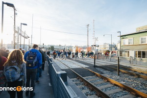 A big group of passengers cross train tracks in Tacoma. Text reads 'connections' with the 'T' emphasized