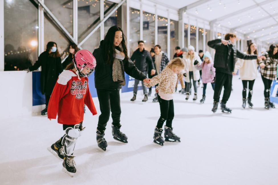 Three people hold hands while ice skating at an outdoor rink in Bellevue