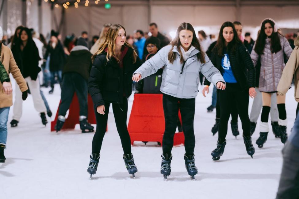 Two young friends hold hands while ice skating