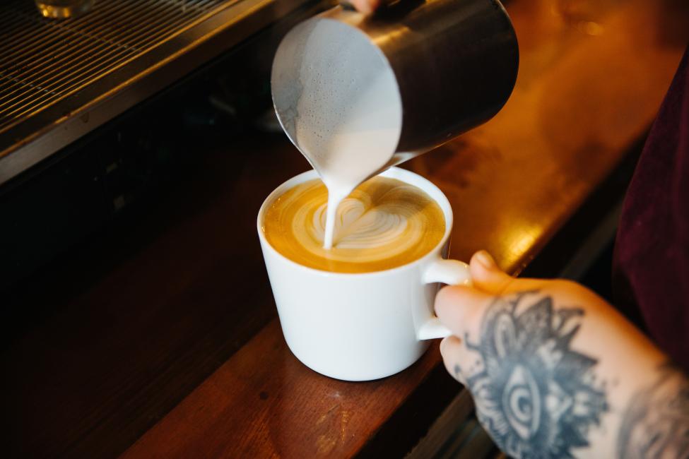 A barista pours milk into a latte