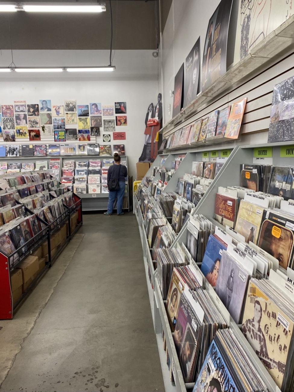 A person stands in a corner of a record store, with vinyls lining the walls