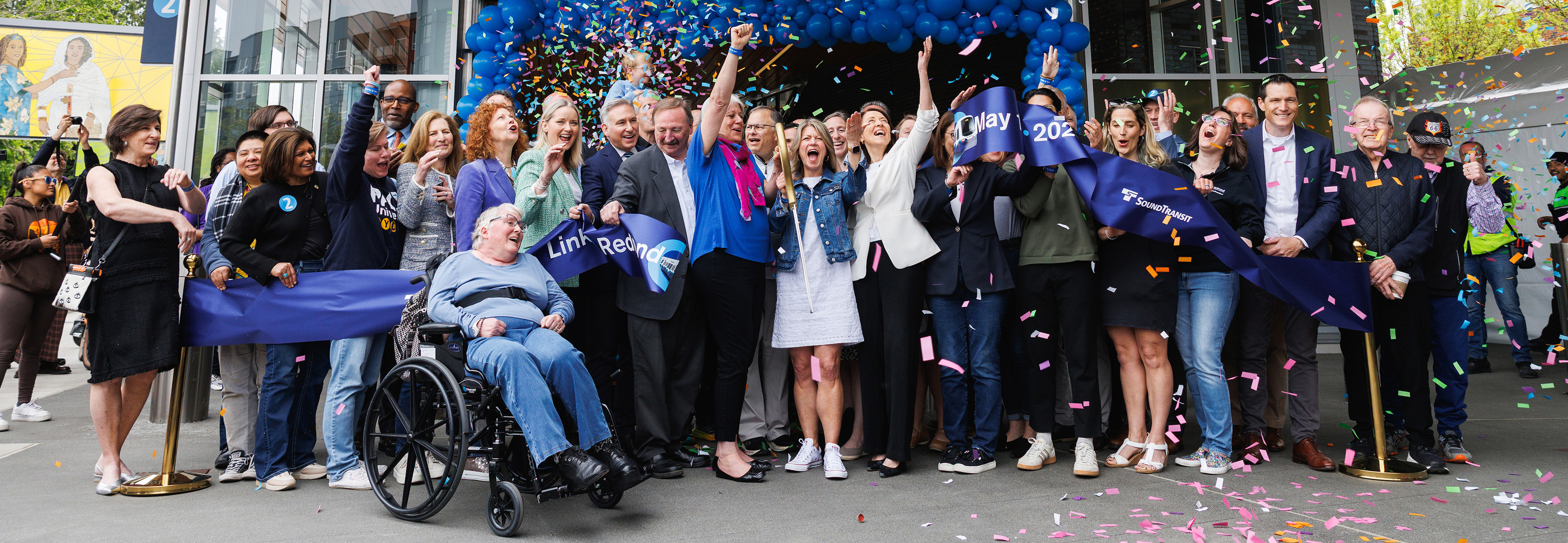 Community members and local elected officials celebrate a light rail extension opening as confetti falls.