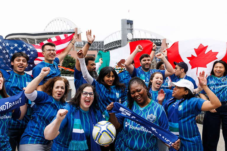 A group of soccer fans cheer while wearing Sound Transit gear.