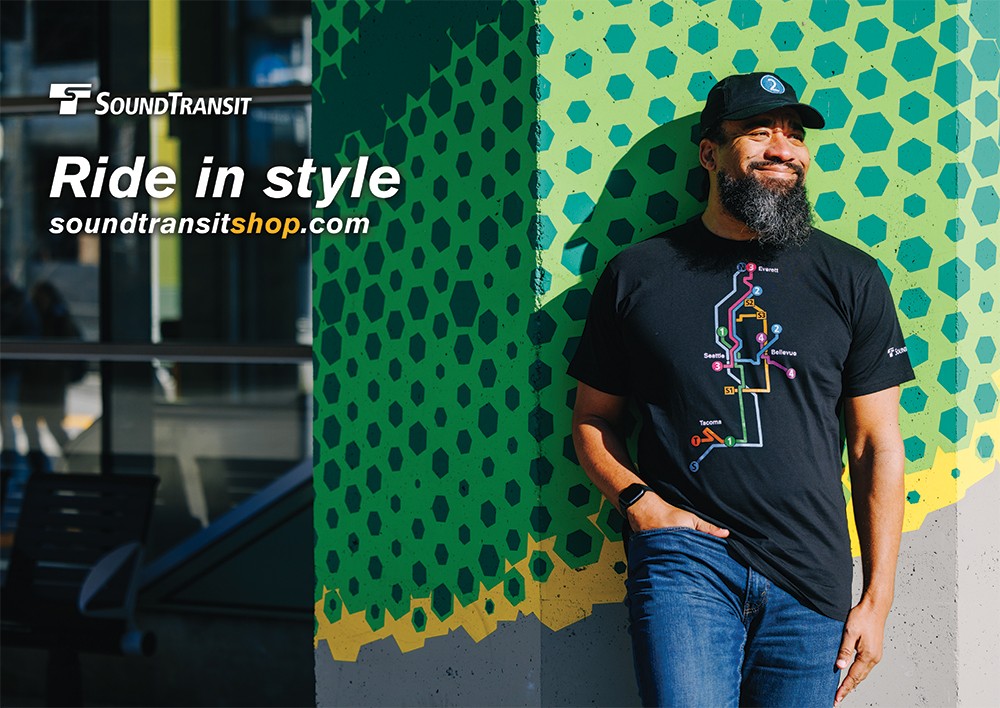 A man leans against a wall wearing a Sound Transit t shirt. Sound Transit Shop: Ride in style at soundtransitshop.com.