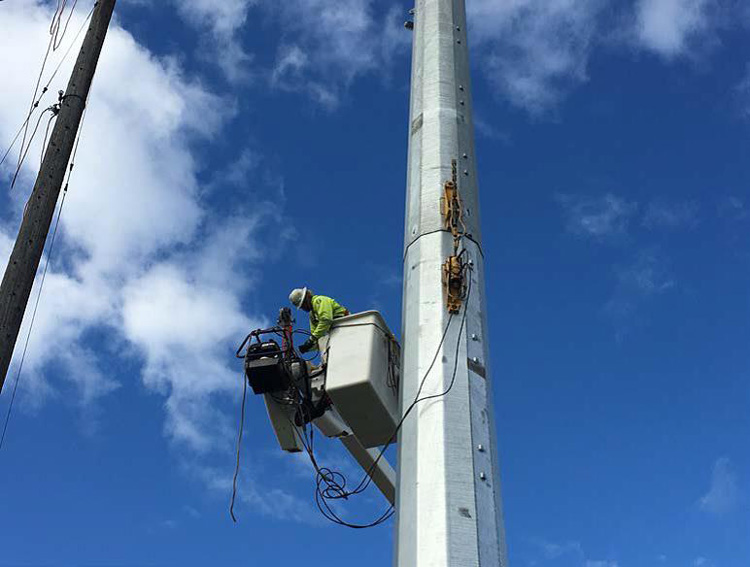 A worker uses hydraulic jacks to pull the electrical pole sections together.