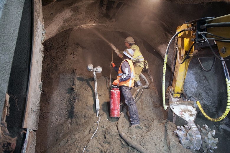 Miners spray a shotcrete mixture onto the exposed soil as the tunnel is excavated