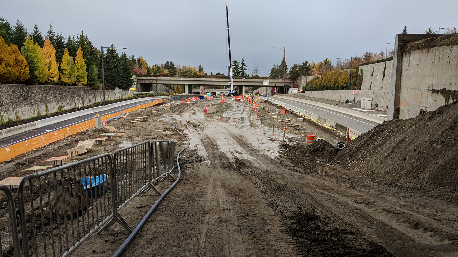 Crews excavate the Mercer Island station area to prepare for sound wall installation. Drilled concrete shafts can be seen to the left and right, and will support the future platform sound walls.