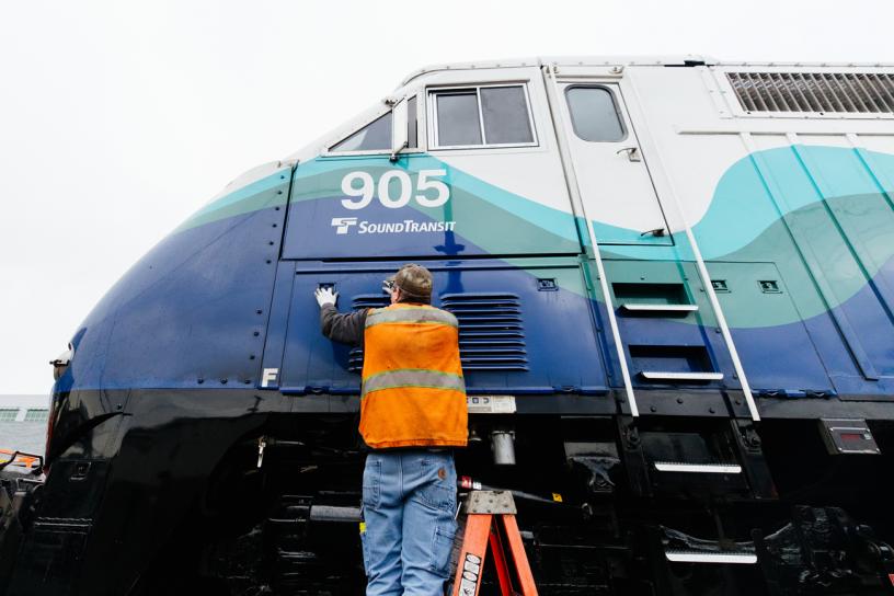 A maintenance crew member closes an access panel to the air filters outside a Sounder train at the Sounder maintenance base in Seattle.