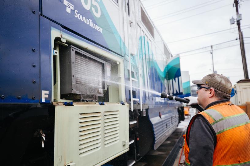 A maintenance crew member cleans air filters with a pressure hose outside of a Sounder train at the Sounder maintenance base in Seattle.