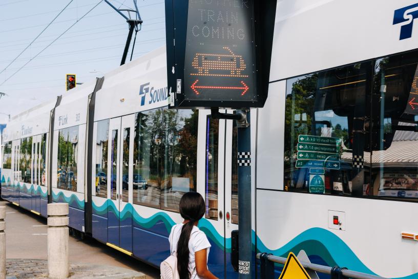 A passenger waits to cross the street while a 1 Line train passes in front of them.