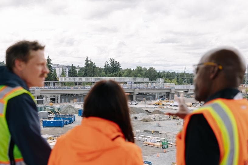 Three people in protective gear look at the construction on the Federal Way Link Extension