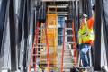 A worker stands on the side of a walkway next to pieces of gear, including orange ladders