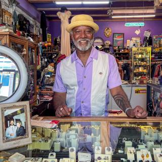 Shop owner of D Haberdashery, Dion Teague, smiling behind the counter
