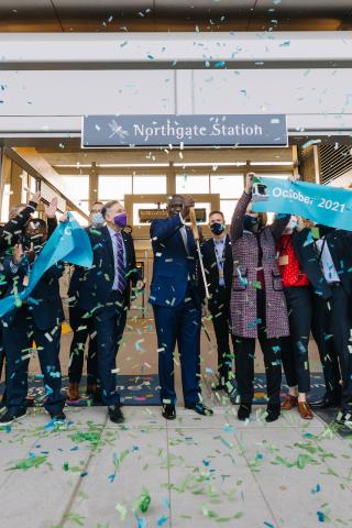 Photo of Sound Transit employees cutting a teal blue ribbon at Northgate Station opening for 1 Line, Northgate Link Extension