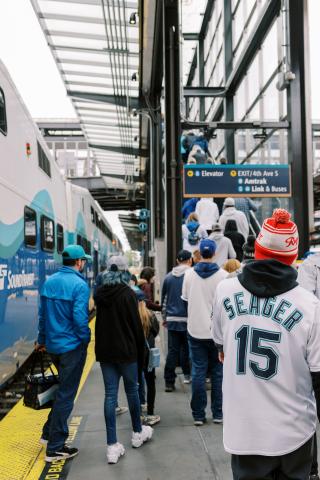 A crowd wearing Mariners gear departs a Sounder train at King Street Station.