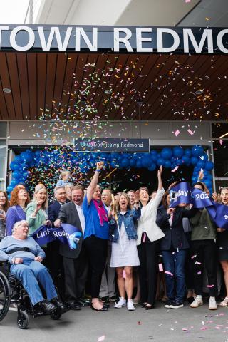 A group of people celebrates the ceremonial ribbon cutting as confetti falls at Downtown Redmond Station.