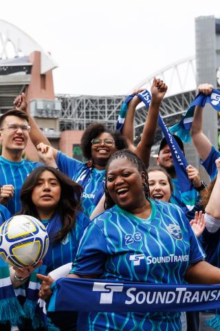 A group of about 10 people wear soccer jerseys and cheer
