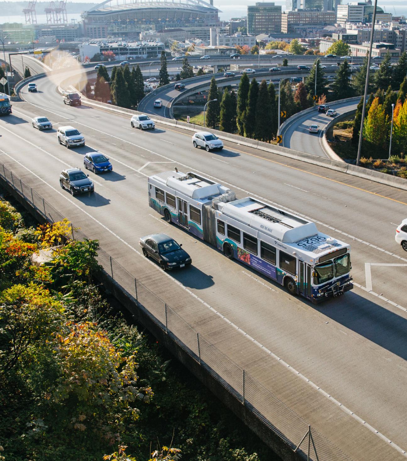 A Sound Transit express bus on the freeway with the Seattle sports stadiums in the distance.
