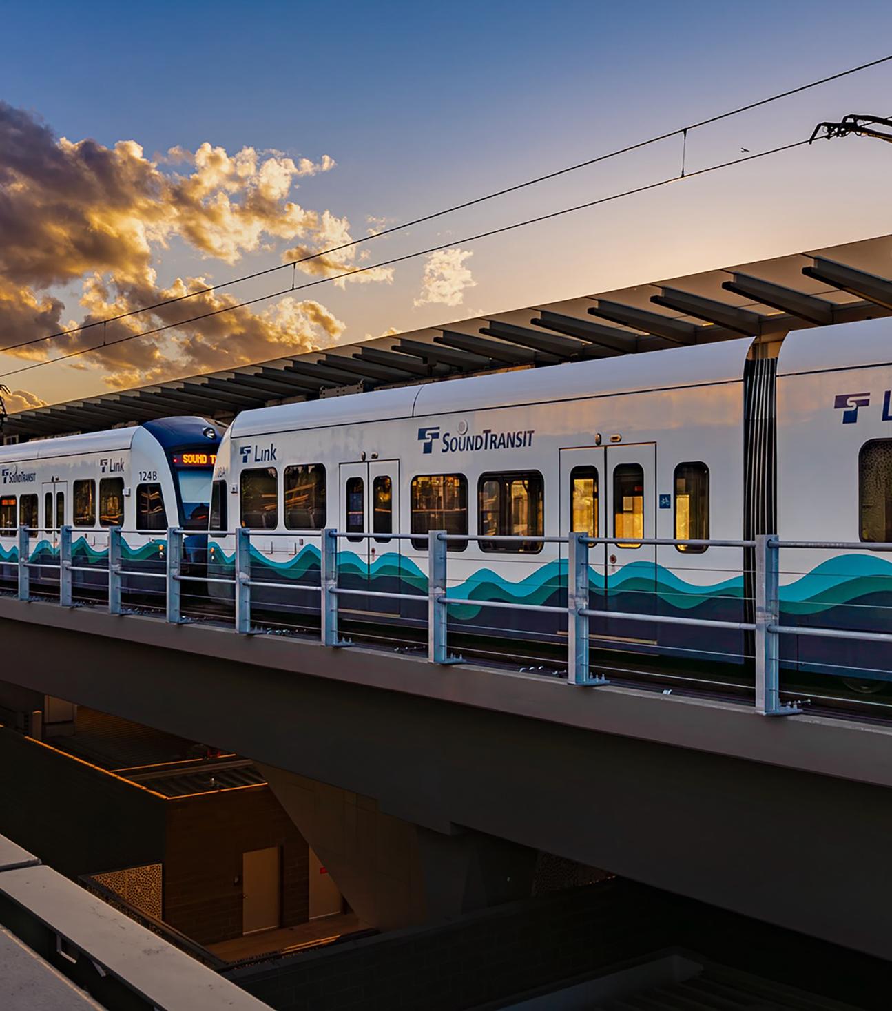 A Link light rail train waits at a station as the sun sets.