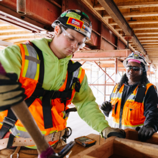 A group of three construction workers with safety gear and tools are shown building the Federal Way Link Extension. 