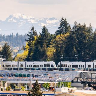 A 2 Line train at Wilburton Station, with trees and mountains in the background and the nearby pedestrian bridge in the front