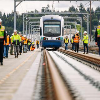 People in protective gear walk next to a Link light rail vehicle on the I-90 bridge during an unpowered tow test.