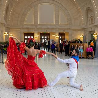Two dancers - one in a long red dress and one in a white suit - perform for a crowd in Union Station