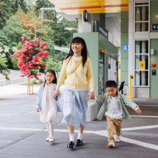 A mom and her two kids hold hands and walk near the entrance to South Bellevue Station on a sunny day