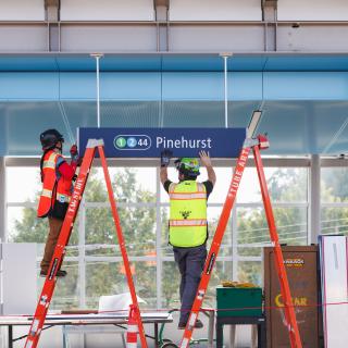 Photo of workers hang the Pinehurst sign at Pinehurst Station