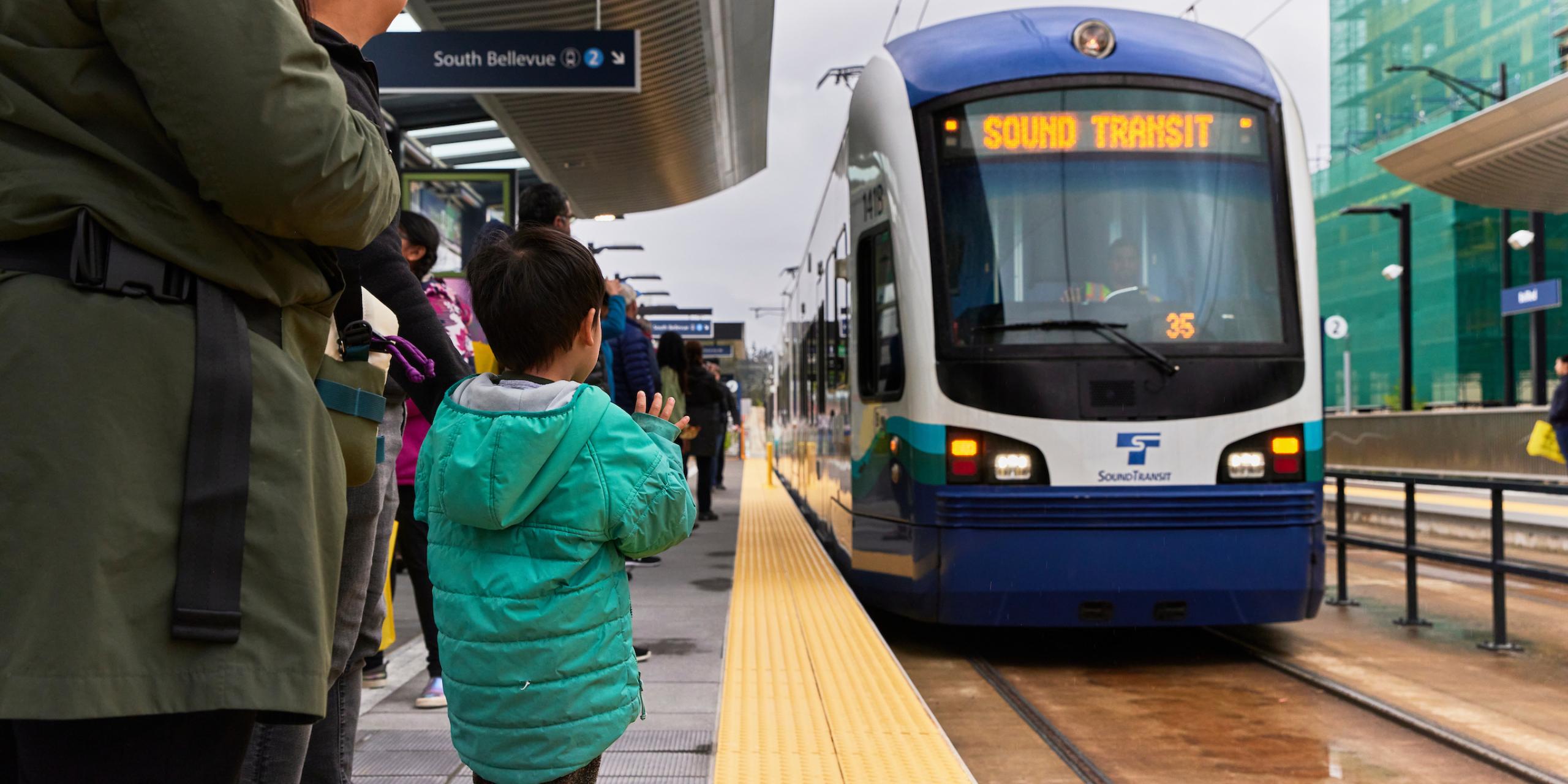 A child in a green jacket waves at the operator of a 2 Line train