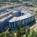 An aerial shot of a mixed-use building right next to the parking garage at Angle Lake Station, with a Link train on the platform in the background