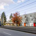 Gray colored housing with red doors on a street with cars and a light rail track. 