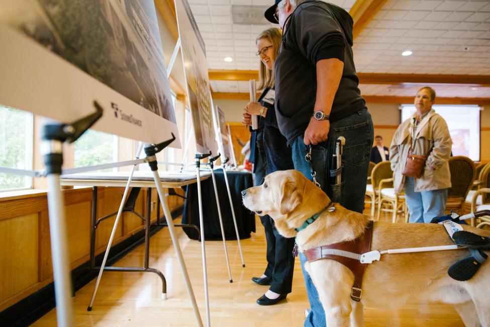 2018 in review: a visually-disabled person asks a Sound Transit staffer to describe the pictures on a display board.