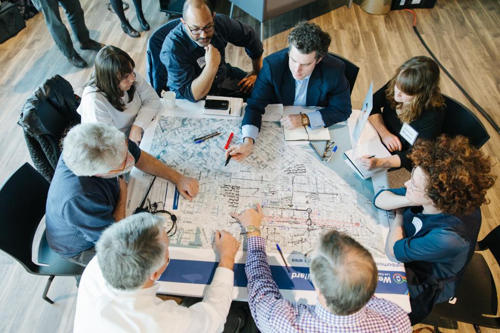 2018 in review: people gather around a map on a table at an outreach meeting about future train lines.