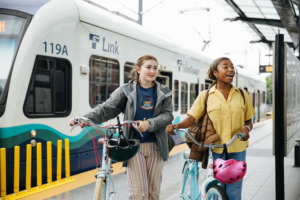 Two teenage girls with bikes walk on the platform at Othello Station. 