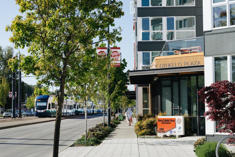 A light rail vehicle passes a building called Mercy Othello Plaza.