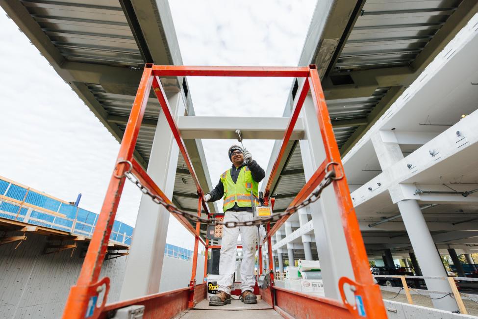 A man in a construction vest and hard hat and standing on a lift paints a structure at Redmond Technology Station.