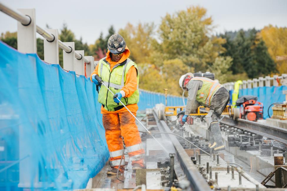 A construction worker sprays water at the rails being installed near Wilburton Station.