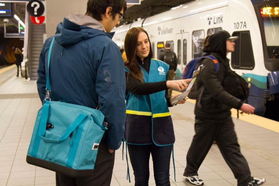 A Sound Transit employee in a blue vest directs a rider on how to use light rail.